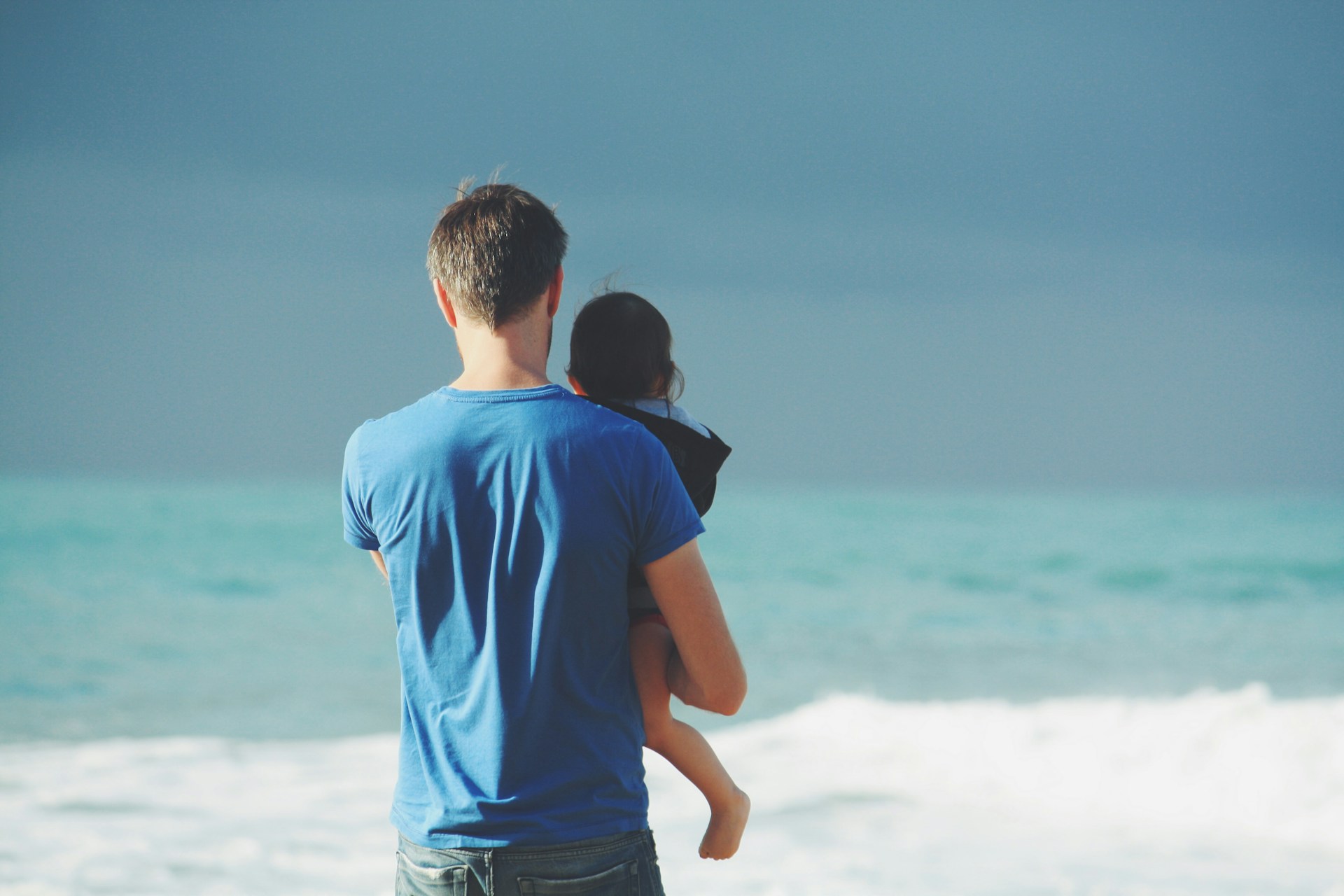 man holding child looking at ocean