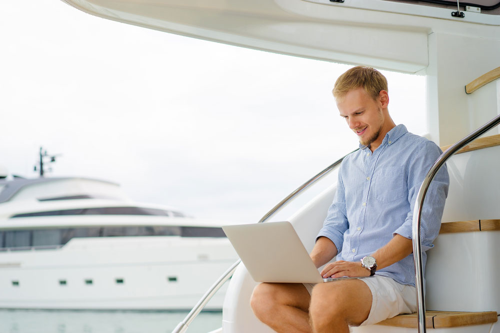 Handsome young man using laptop on the deck of modern yacht